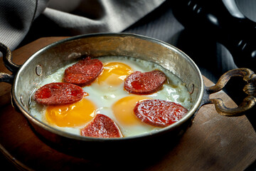 Appetizing turkish breakfast dish - scrambled eggs with sujuk in a frying pan on a black background