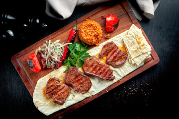 Grilled beef fillet with bulgur and vegetables garnished on a wooden board. Turkish kebab. Close up, selective focus