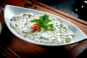 Traditional Arabian eggplant dish Baba Ghanoush with olive oil and herbs in white yogurt. Wood table. Close up