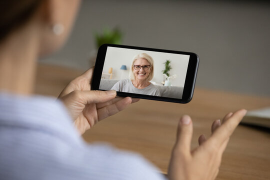 Back view of woman talk speak on video call on smartphone gadget with smiling elderly Caucasian mom. Female have webcam digital online conversation on cellphone with mother. Communication concept.