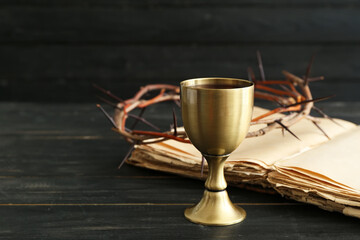 Chalice of wine with Holy Bible and crown of thorns on dark wooden background