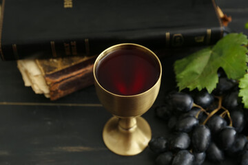Chalice of wine with Holy Bible on dark wooden background