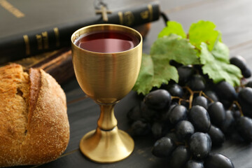 Chalice of wine with bread and Holy Bible on dark wooden background