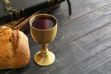 Chalice of wine with bread and Holy Bible on dark wooden background