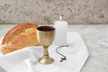Chalice of wine with bread, cross and candle on grey background