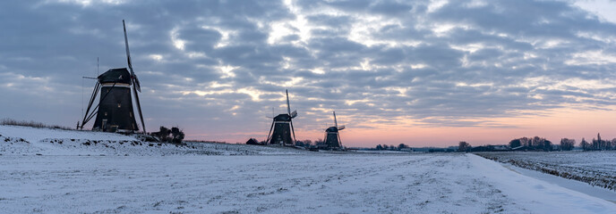 Panorama photo of a sunrise on a cold winter morning with a snowy landscape at the three windmills...