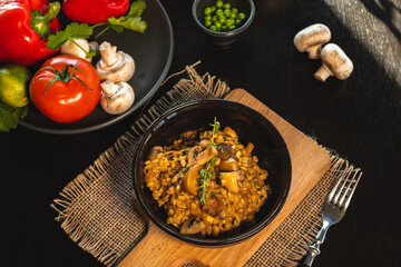 Pearl barley risotto or orzotto with mushrooms in dark bowl on wooden background. Selective focus.