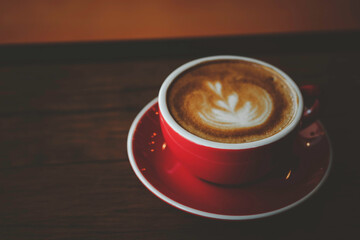Red cup hot coffee latte on wood bar in coffee shop cafe.