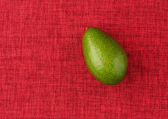 Avocado. The ripe fruit is green, on a red background
