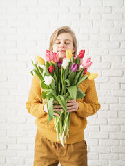 Happy beautiful woman in yellow clothes holding bouquet of tulips