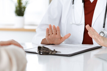 Unknown woman-doctor and patient discussing something while sitting at the table in clinic, close-up. Medicine concept
