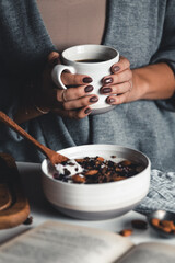 A young woman drinks morning coffee, eats a healthy breakfast and reads a book. Morning routine. Stylish manicure. Correct habits. Holding a cup in his hands