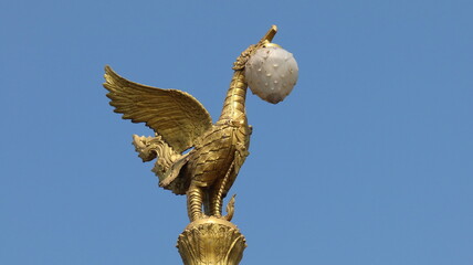 Fototapeta na wymiar Swan-like golden lamp post soars into blue sky