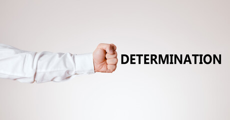 Businessman arm with hand as a clenched fist points towards the word determination.