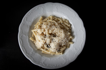 Macaroni With Grated Cheese And Black Sesame Seeds On A White Plate On Dark Brown Background