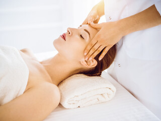 Obraz na płótnie Canvas Beautiful woman enjoying facial massage with closed eyes in sunny spa center