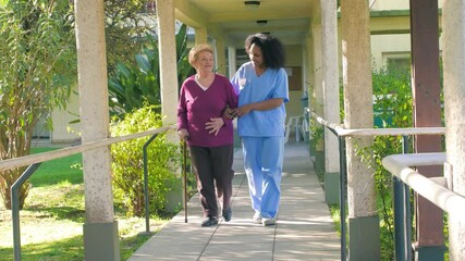 African doctor helps elderly woman with walker in the hospital garden patio - Slow motion