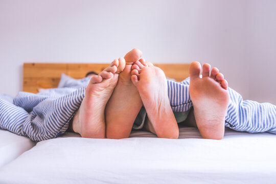 Couple is enjoying the morning in bed: Close up of uncovered feet in the bed, blanket - Powered by Adobe
