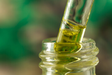 Jojoba oil is drawn from a glass bottle using a pipette. Bubbles of oil in a pipette close-up. Dropper with oil on a green background.