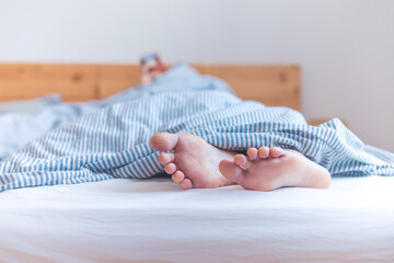 Couple is enjoying the morning in bed: Close up of uncovered feet in the bed, blanket