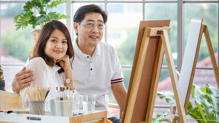 Senior man and woman couple, husband and wife, painting image together in home gallery with warm and happy circumstance. The man holds woman with love and care.