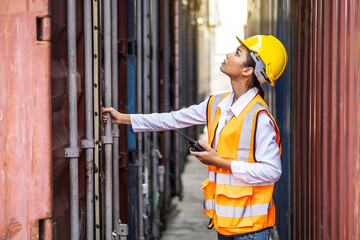 Young confident woman engineer using radio communication and wearing yellow safety helmet and check for control loading containers box from Cargo freight ship for import and export