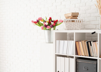 Bucket of tulip flowers next to the bookshelf over white brick wall background