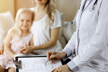 Obraz premium Doctor and patient. Pediatrician using clipboard while examining little girl with her mother at home. Happy cute caucasian child at medical exam. Medicine concept