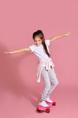 cute happy little child girl riding skateboard against pink background.