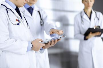 Group of unknown doctors use a computer tablet to check up some medical names records, while standing in a hospital office. Physicians ready to examine and help patients. Medical help, insurance in