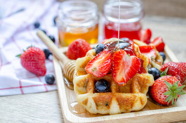 Fresh honey puring on strawberry and blueberry fruit on top of delicious homemade waffle in wooden dish ready for breakfast meal