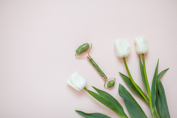 Layout with delicate white tulips and jade facial massager on light pink background. High quality photo
