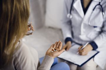 Close-up woman-patient holding pills near her doctor, time to take medications, cure for headache or remedy pain killer drugs. Stay at home concept during Coronavirus pandemic and self isolation