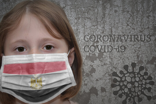 Little girl in medical mask with flag of egypt stands near the old vintage wall with text coronavirus, covid, and virus picture.