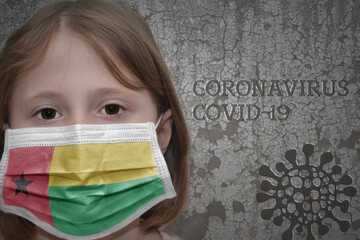 Little girl in medical mask with flag of guinea bissau stands near the old vintage wall with text coronavirus, covid, and virus picture.