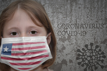 Little girl in medical mask with flag of liberia stands near the old vintage wall with text coronavirus, covid, and virus picture.