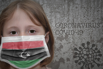 Little girl in medical mask with flag of libya stands near the old vintage wall with text coronavirus, covid, and virus picture.