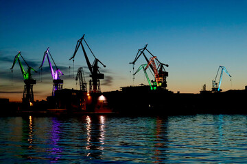 Fotografie von dem Farbspiel der Kr&auml;ne in Pula in Kroatien bei Nacht vor einem strahlen blauen Nachthimmel..