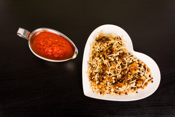 Famous traditional Arabic, Egyptian dish - Koshari. National Kushari in a white plate on dark wooden background with tomato sauce top view
