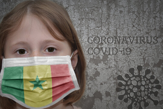 Little Girl In Medical Mask With Flag Of Senegal Stands Near The Old Vintage Wall With Text Coronavirus, Covid, And Virus Picture.