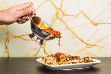 Famous traditional Arabic, Egyptian dish - Koshari. National Kushari in a white plate on dark wooden background with hand dropping tomato sauce