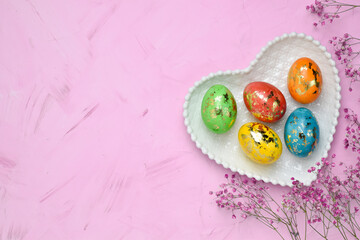 Five Easter eggs lie in a plate with a heart on a delicate background. Postcard with eggs on a pink...