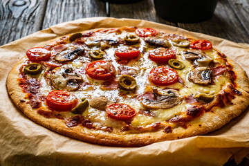 Pizza with champignons, ham, tomatoes, olives, parmesan and mozzarella on wooden background
