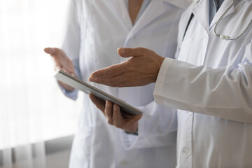 Crop close up of medical specialists in white uniforms hold use modern tablet gadget brainstorm sickness or prescription. Diverse doctors cooperate work together on pad device in clinic or hospital.