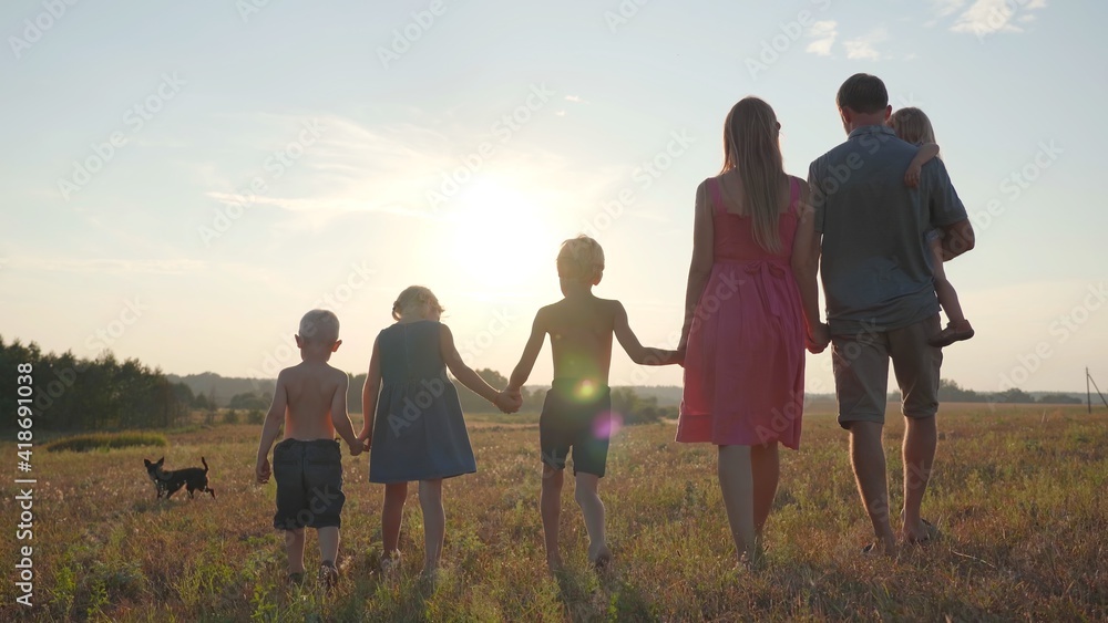 Wall mural a friendly large family walks across the field at sunset.