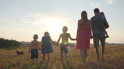 A friendly large family walks across the field at sunset.