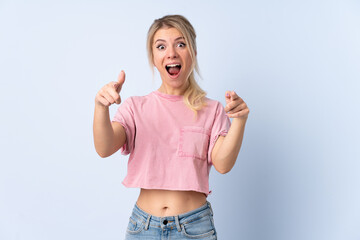 Blonde woman over isolated blue background surprised and pointing front