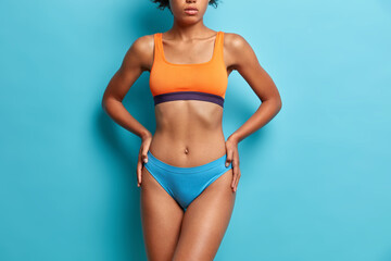 Cropped shot of healthy slim woman dressed in top and pants has perfect figure after dieting feels beautiful has sporty body isolated over blue background