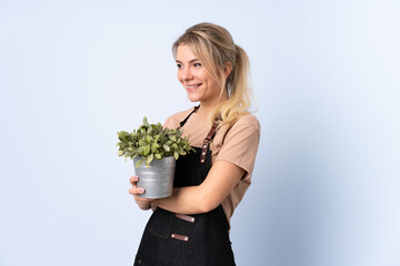 Blonde gardener woman holding a plant over isolated background looking to the side