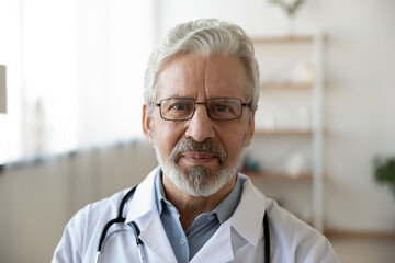 Headshot portrait of mature Caucasian male doctor in glasses wear white medical uniform look at...